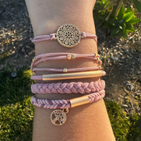 Close-up of a wrist wearing multiple pink and gold bracelets with decorative charms against a natural background.