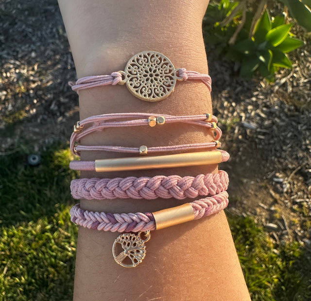 Close-up of a wrist wearing multiple pink and gold bracelets with decorative charms against a natural background.