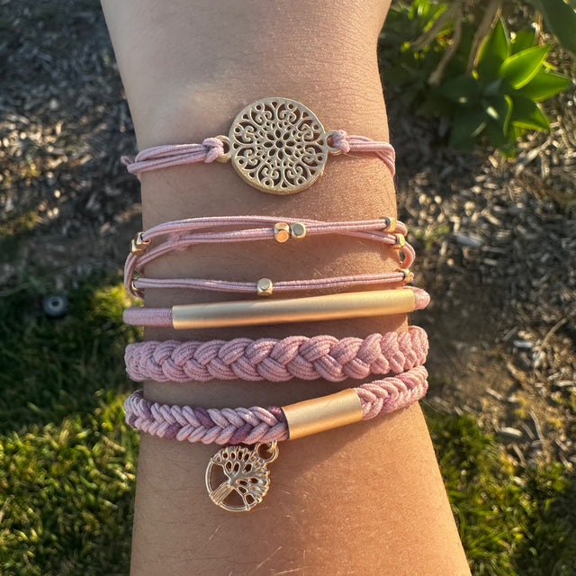 Close-up of a wrist wearing multiple pink and gold bracelets with decorative charms against a natural background.